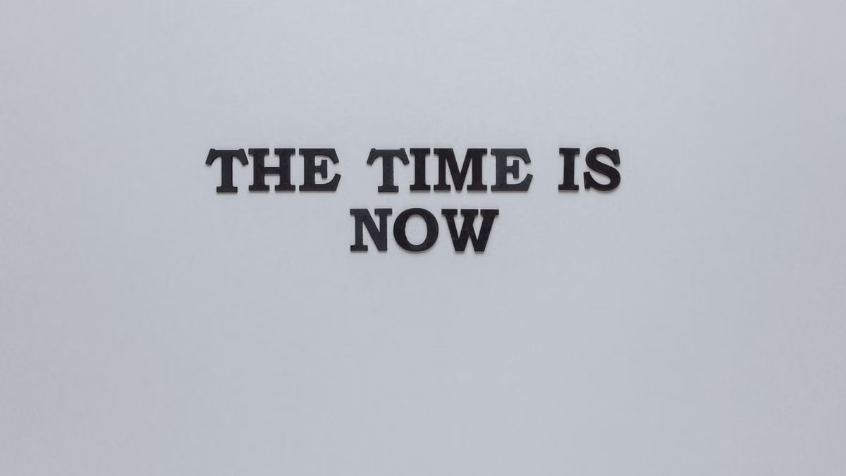 Minimalist poster with the motivational quote 'The Time is Now' on a gray background.